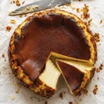 Basque burnt cheesecake with a caramelized brown top and creamy sliced center on parchment paper.