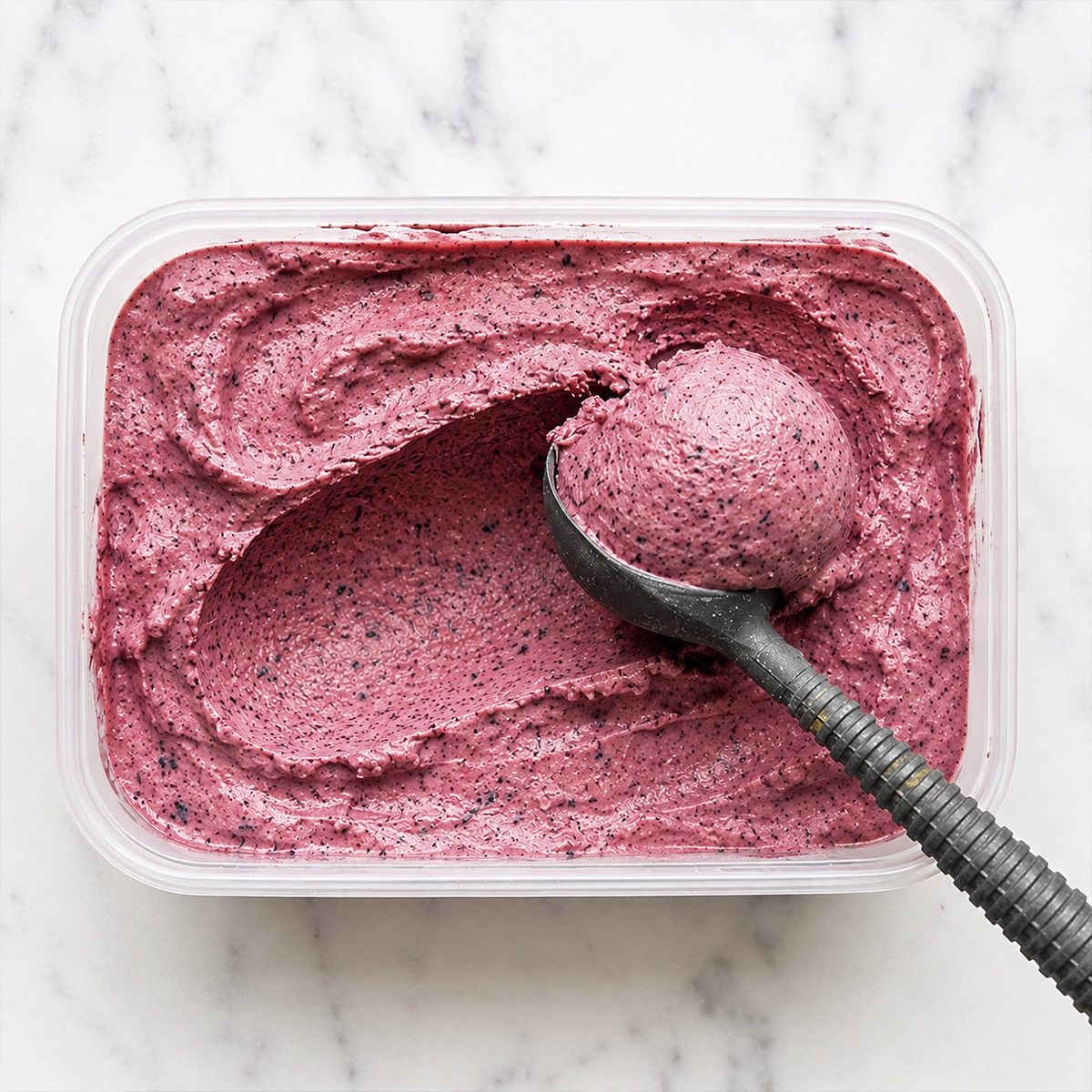 Creamy homemade mixed berry frozen yogurt with a fresh scoop and dark berry flecks in a freezer container.