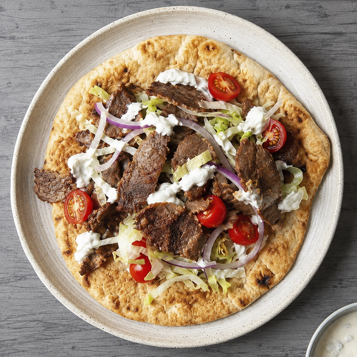 Thin crispy beef pieces on grilled pita with shredded lettuce, tomatoes, red onion, and yogurt sauce
